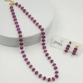 Purple beaded necklace with gold accents on a white surface, accompanied by a matching earring set on a branded card.