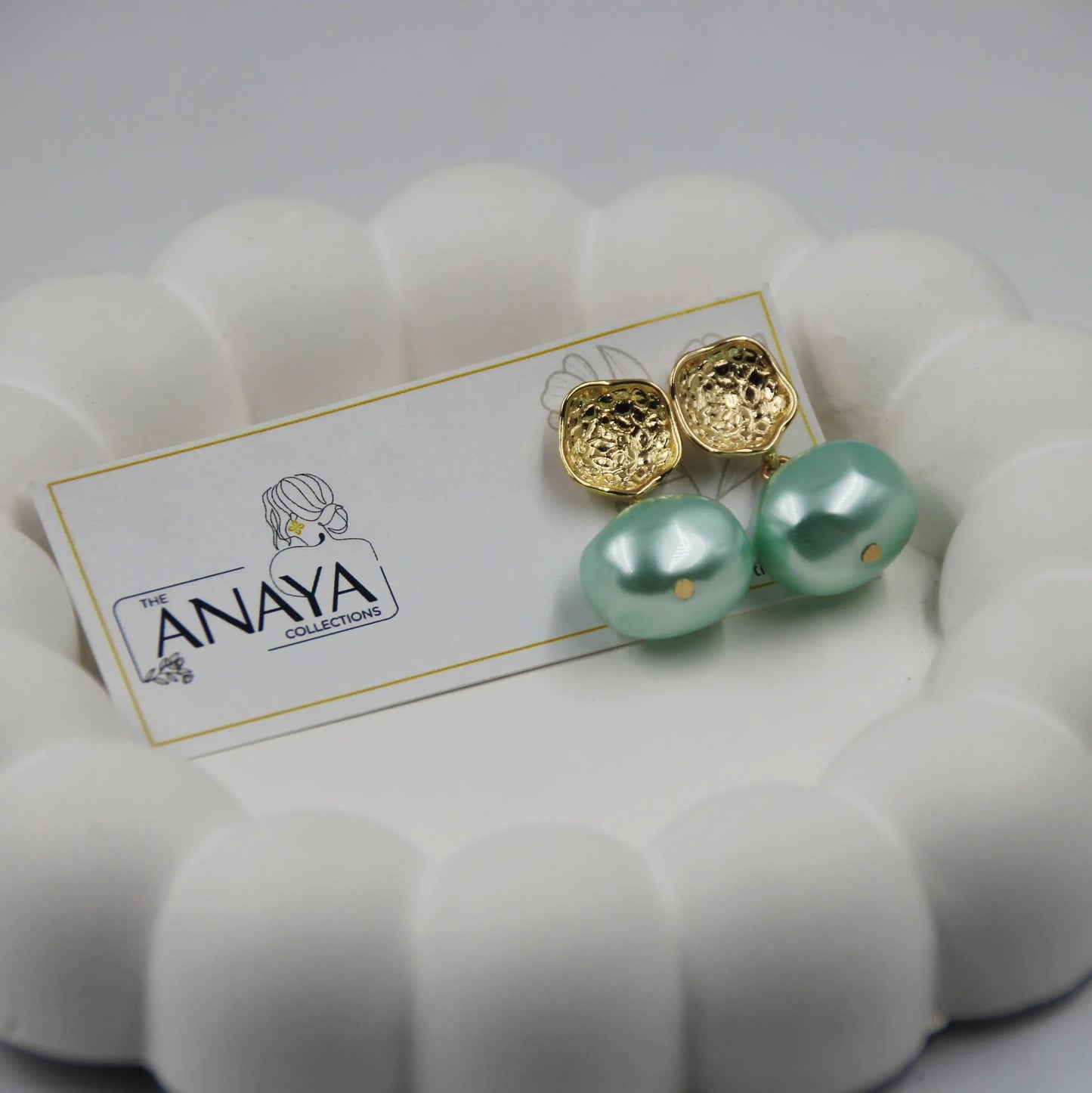 Gold and green pearl earrings on a branded card with a white background