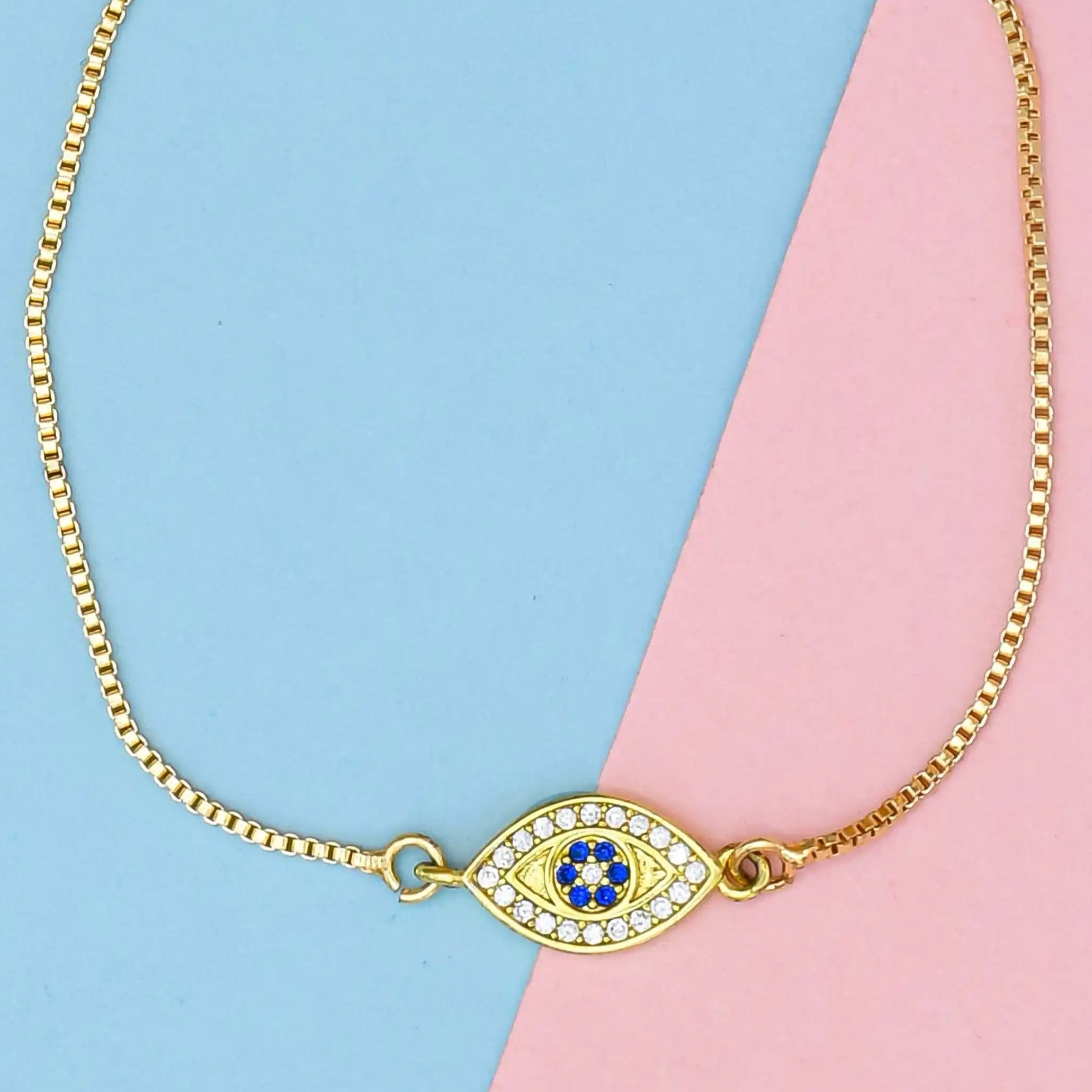 Gold bracelet with an eye-shaped charm on a blue and pink background