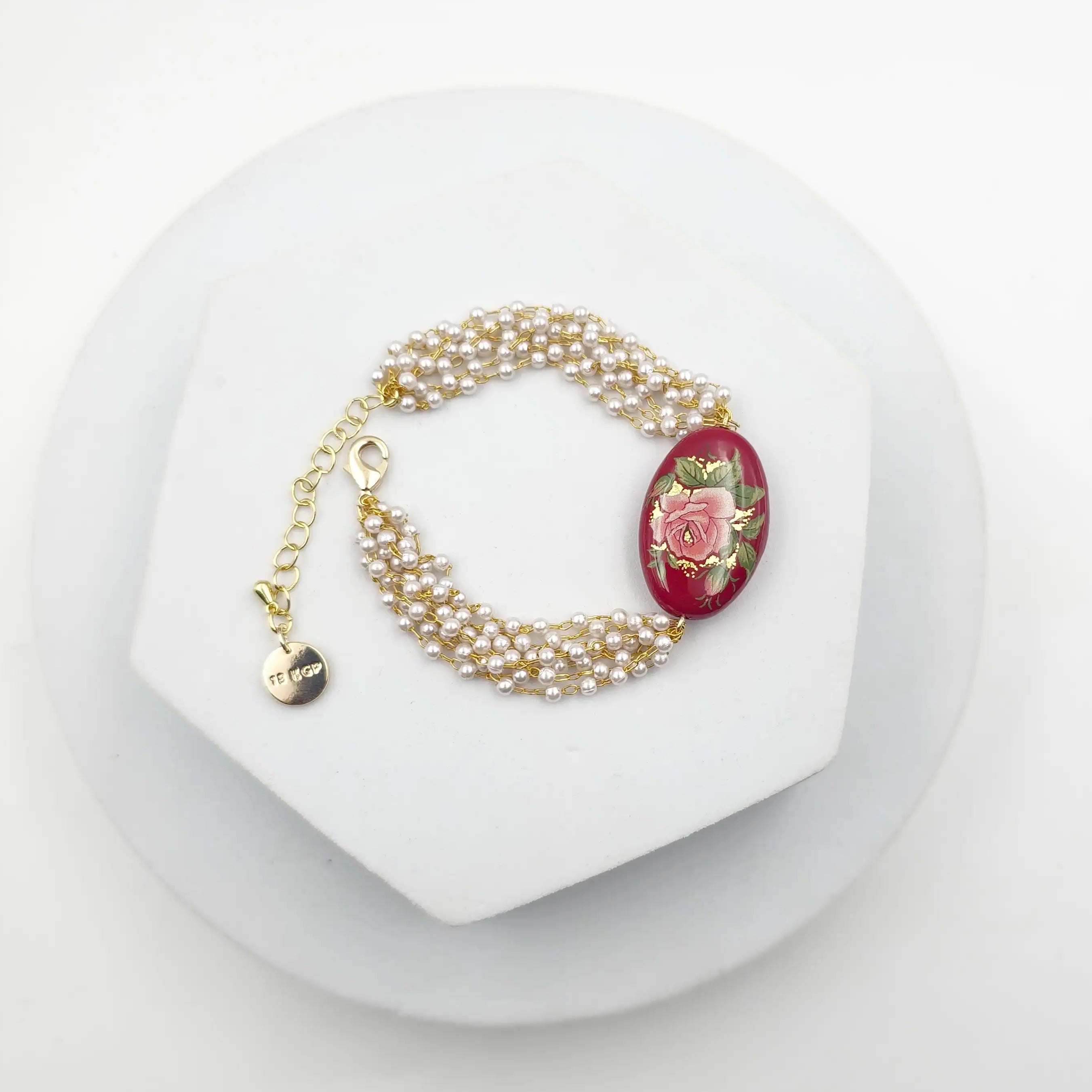 Pearl bracelet with a red flower charm on a white stand
