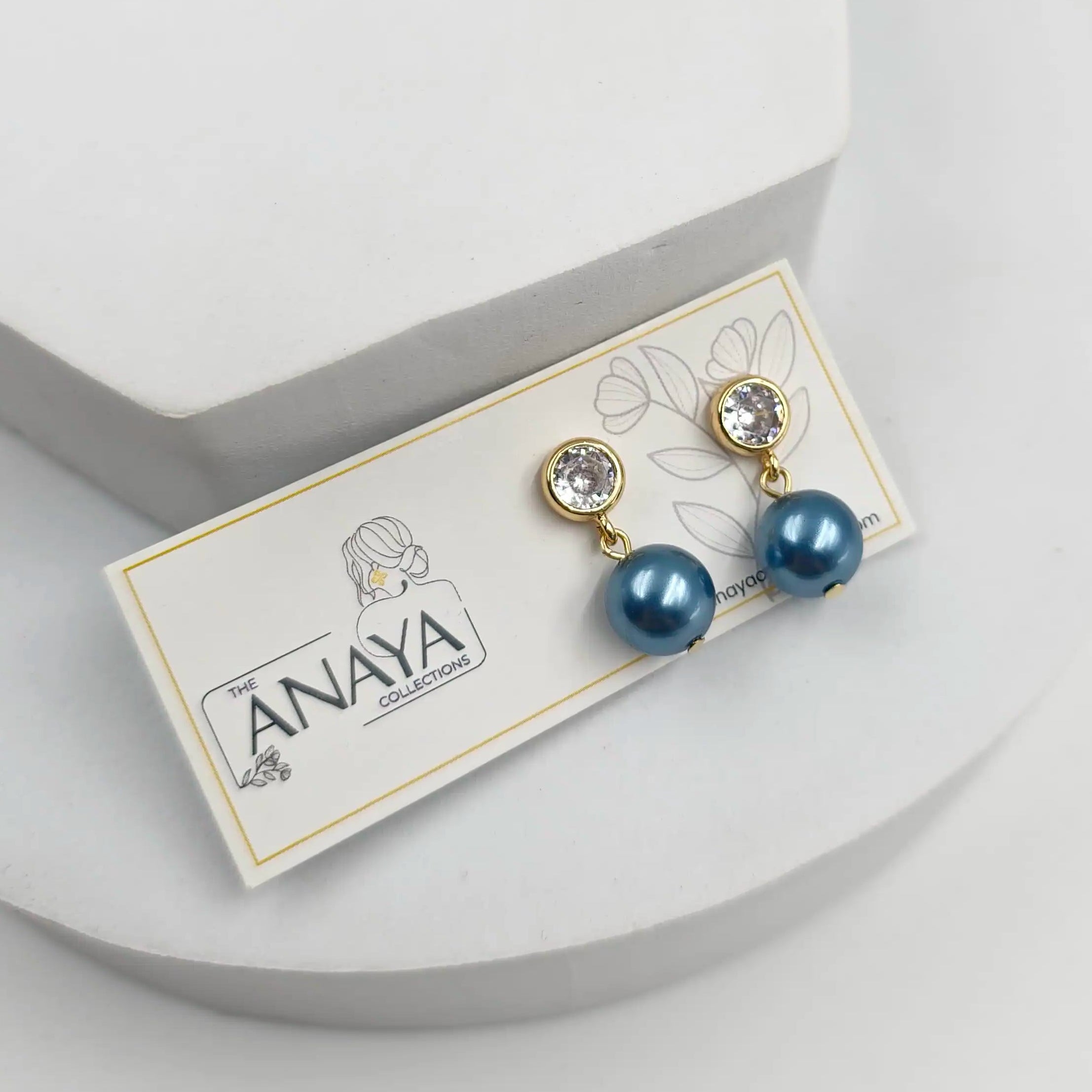 Pair of blue pearl earrings on a branded card against a light gray background
