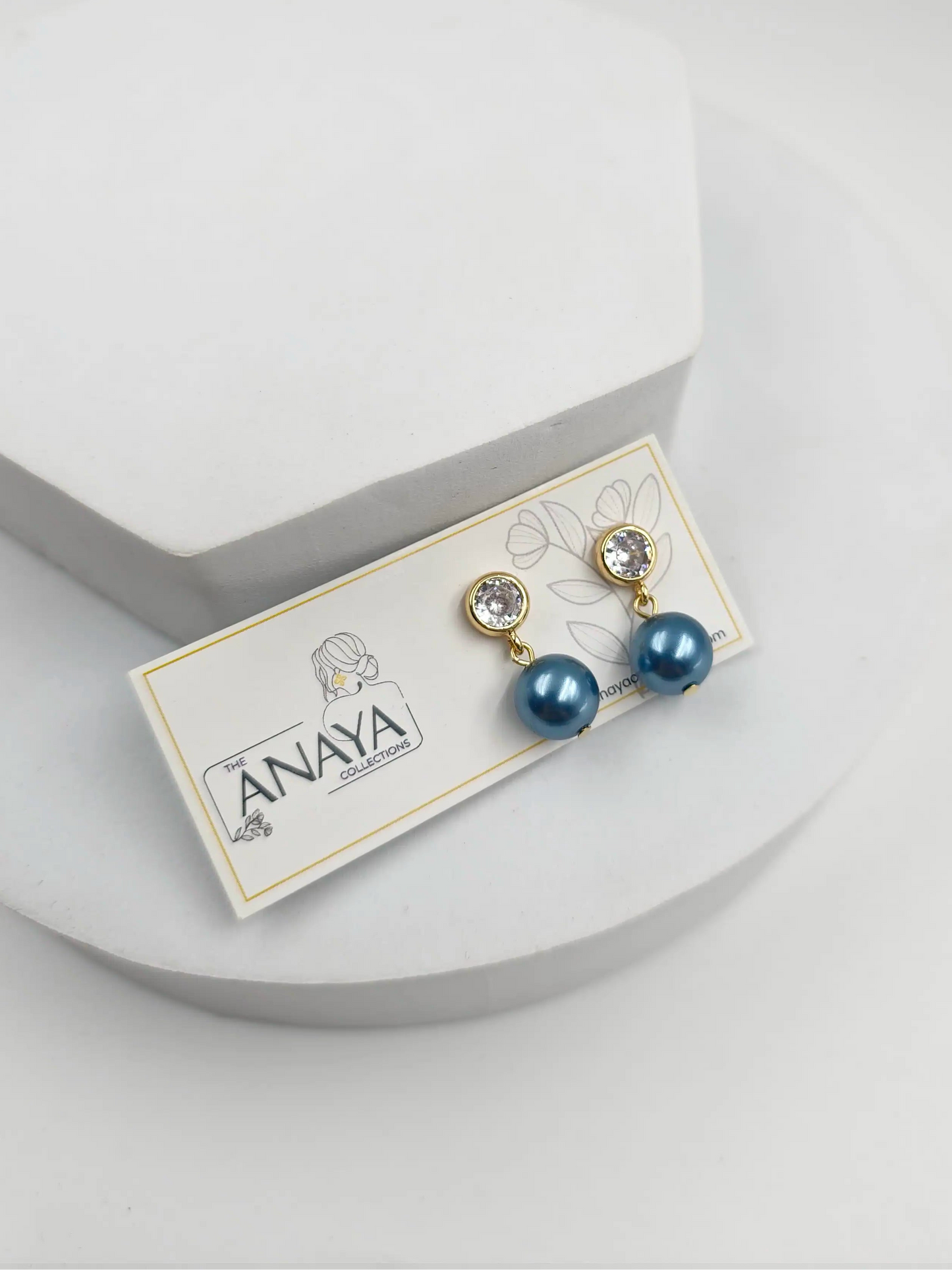 Pair of blue pearl earrings on a branded card against a light gray background