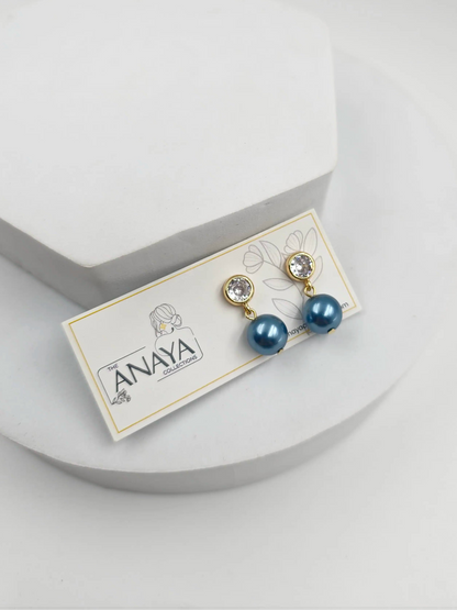 Pair of blue pearl earrings on a branded card against a light gray background