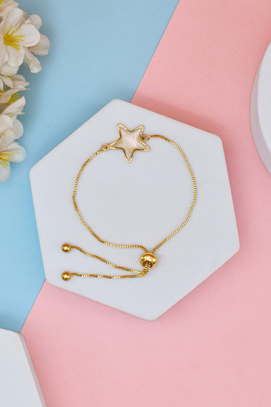 A gold-colored bracelet with a star-shaped charm, displayed on a white stand with a pastel background.