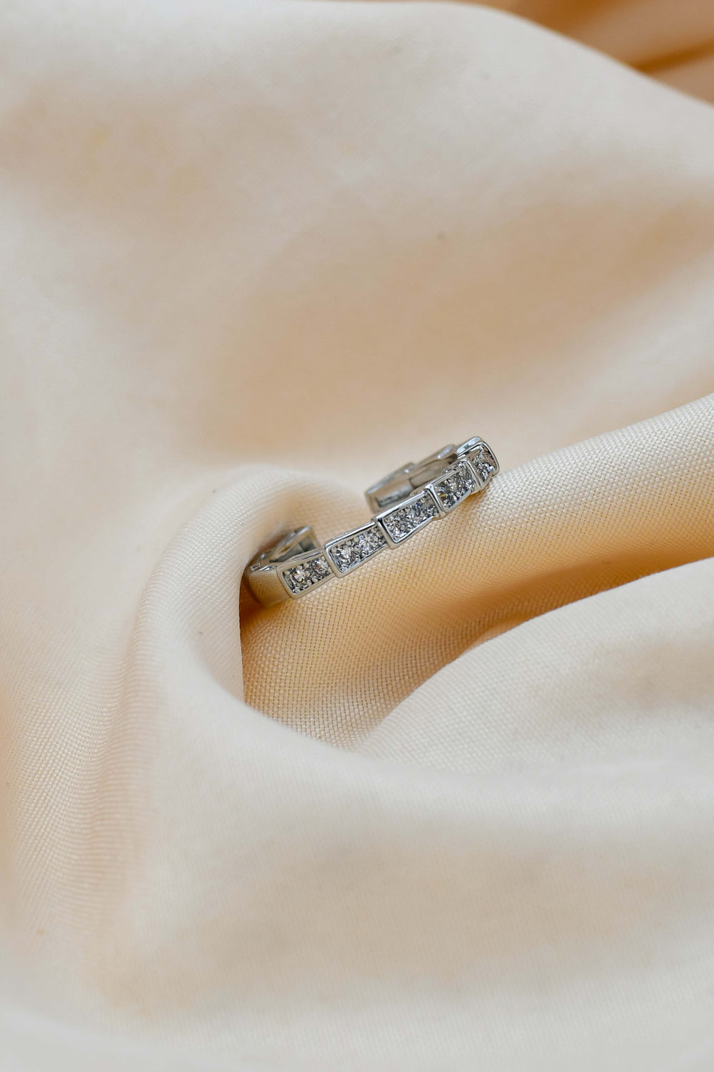 A ring with a sliced design, featuring a band with multiple stones set in a white gold or platinum band, resting on a beige fabric.